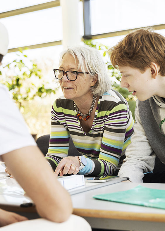 Gymnasielærer sidder ved et bord og taler med to elever