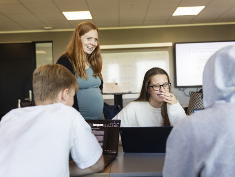 Gymnasielærer står ved et bord og snakker med tre elever