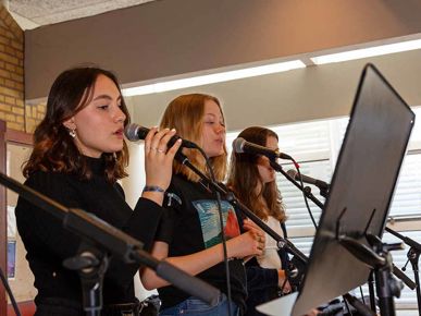 Tre elever står og synger i mikrofoner i et musiklokale 