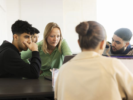 Gymnasielærer hjælper elever med en opgave på en computer